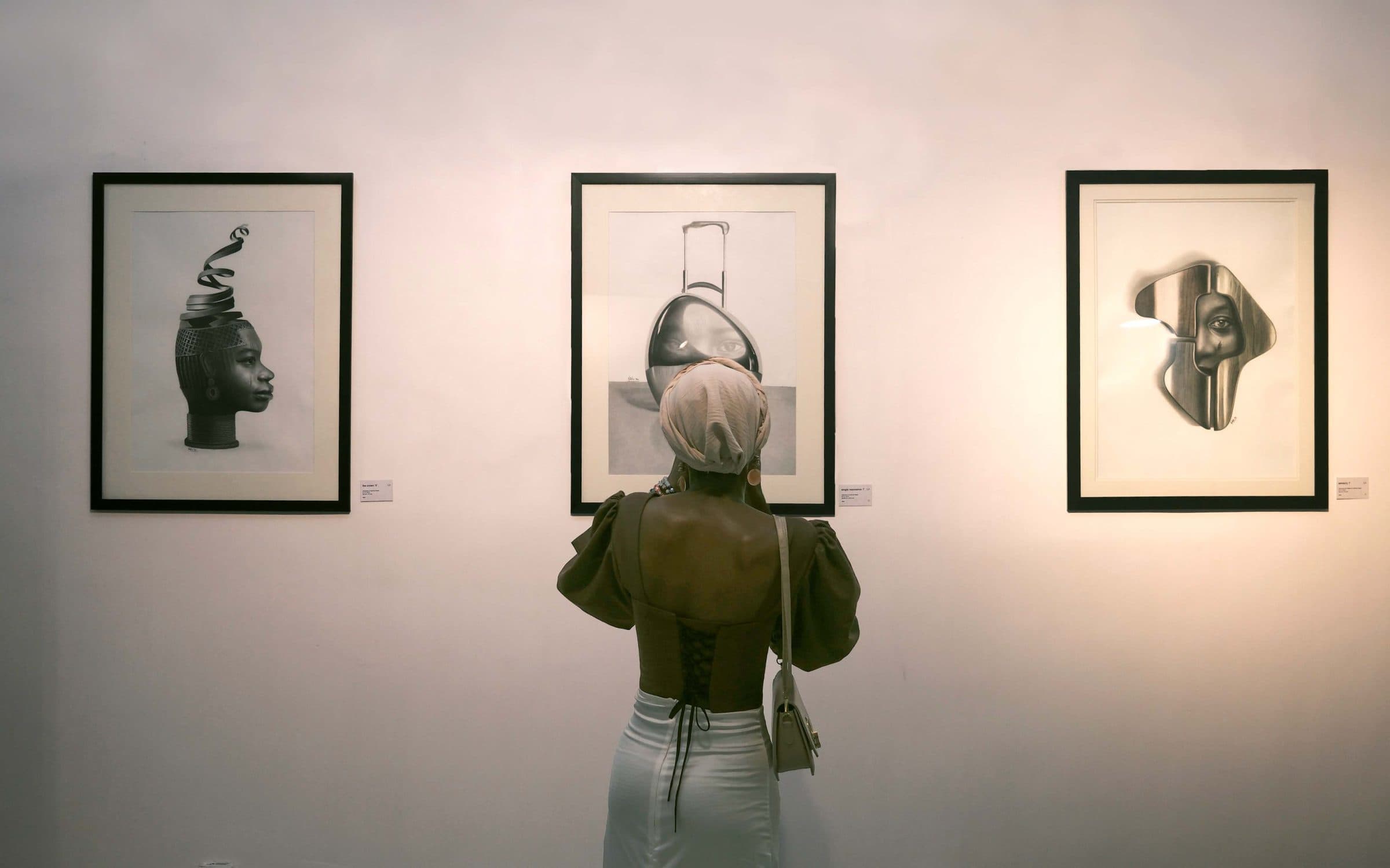 A visitor in green looks at three framed works