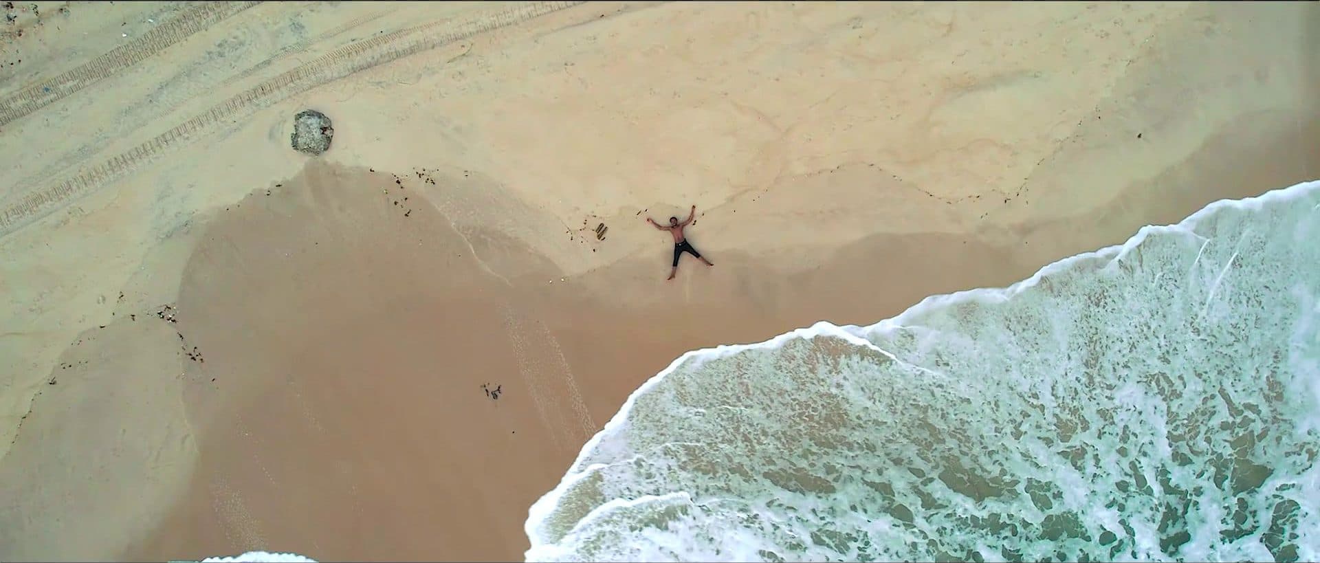 An aerial view of a figure lying on a beach by the sea