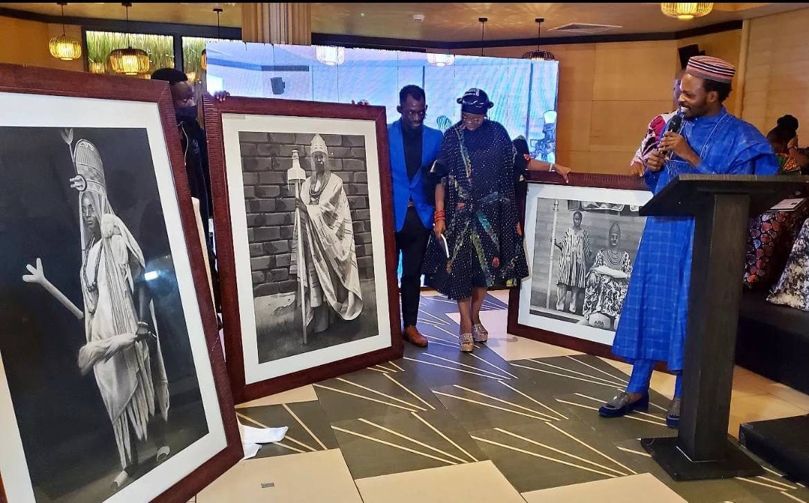 A speaker addresses guests beside framed portraits of female kings