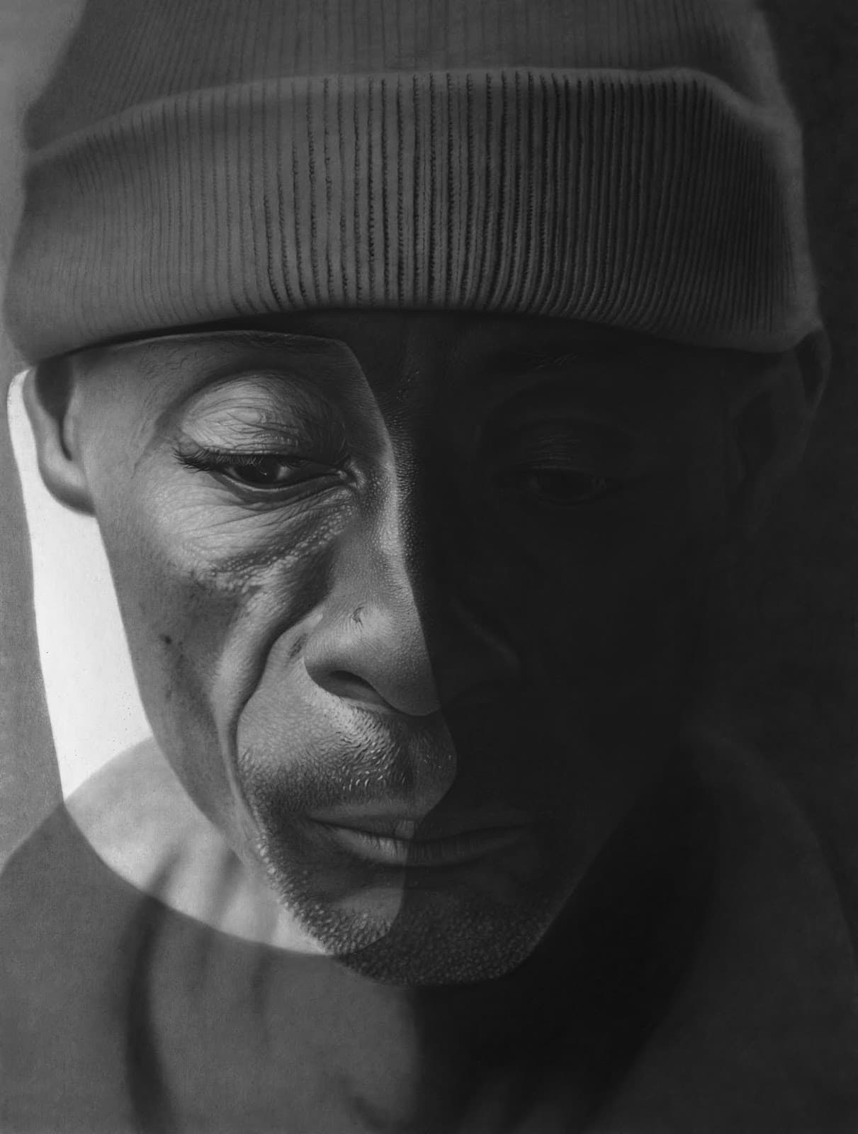 Charcoal portrait of an older man in a knit cap, half his face in shadow